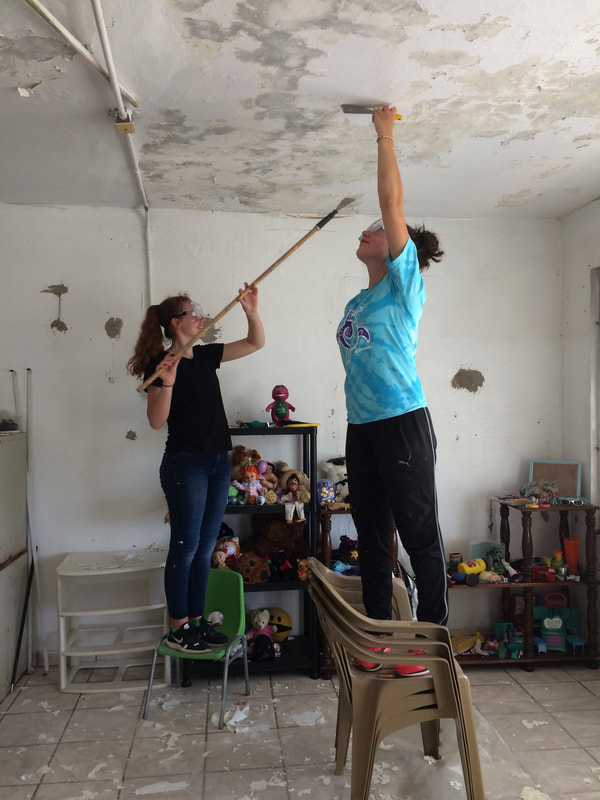 two youths repairing the ceiling in a room, with children's toys in the background